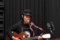 Musisi Jhon Selno bernyanyi sambil memainkan gitar dalam rekaman Podcast Kusieh Bendi. (Foto: Dok. Podcast Kusieh Bendi)