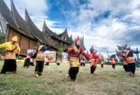Pentas seni tradisional randai Minangkabau di lapangan dengan rumah adat beratap gonjong di belakangnya. (Foto: Dok. Wikimedia Commons/Deni Dahniel (CC BY-SA 4.0))